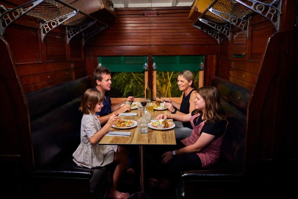 Family sat in an old rail carriage eating dinner at Undara Experience
